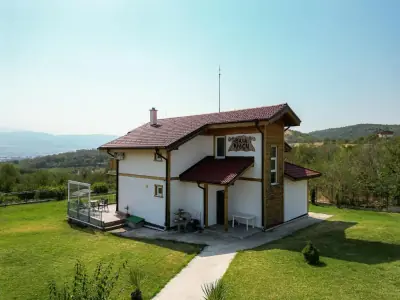 Two-story wooden guesthouse 'Vila Araku' with red roof, covered veranda and outdoor seating