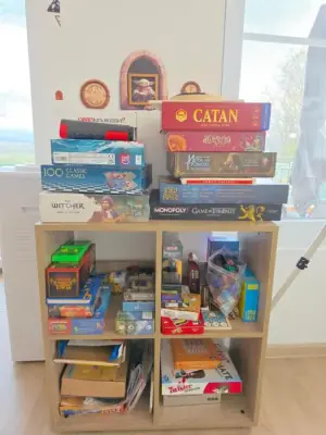 Stacked board games on wooden shelf including Catan and Monopoly