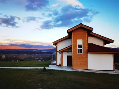 Two-story wooden house with red roof overlooking grassy lawn