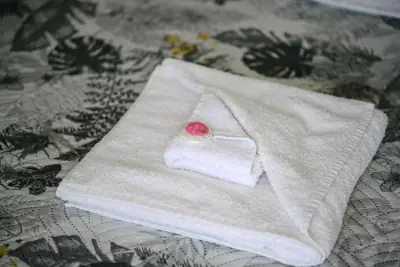 Folded white towel with welcome soap on tropical-print bed